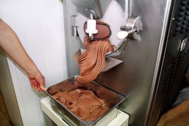 Pudra Şef üniforma içinde Ice cream maker makina üzerinde çalışıyor. Siyah çikolatalı dondurma lezzeti ve üreten çelik konteyner içine düşüyor. İtalyan kremalı dondurma endüstriyel hazırlanması.