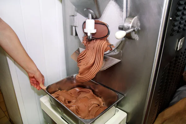 Pudra Şef üniforma içinde Ice cream maker makina üzerinde çalışıyor. Siyah çikolatalı dondurma lezzeti ve üreten çelik konteyner içine düşüyor. İtalyan kremalı dondurma endüstriyel hazırlanması.