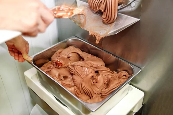 Pudra Şef üniforma içinde Ice cream maker makina üzerinde çalışıyor. Siyah çikolatalı dondurma lezzeti ve üreten çelik konteyner içine düşüyor. İtalyan kremalı dondurma endüstriyel hazırlanması.
