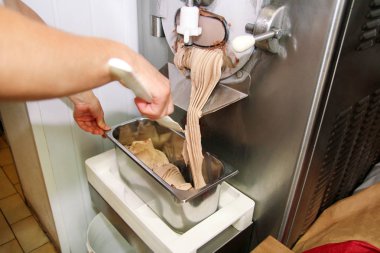 Pudra Şef üniforma içinde Ice cream maker makina üzerinde çalışıyor. Kadın fındık aromalı dondurma üreten, çelik kap içine düşüyor. İtalyan kremalı dondurma endüstriyel hazırlanması.
