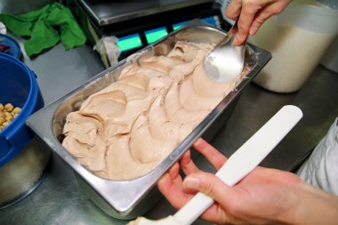 Dondurma fabrikasında çalışan kadın parçalar, parçalar ve fındıklı çelik kap içinde meyvesi ile fındık aromalı kremalı dondurma süsle. Dondurulmuş dondurma ile tepsisinde fındık dökme.