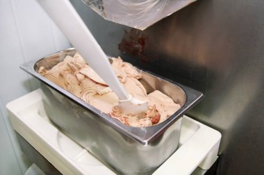 Pudra Şef üniforma içinde Ice cream maker makina üzerinde çalışıyor. Kadın fındık aromalı dondurma üreten, çelik kap içine düşüyor. İtalyan kremalı dondurma endüstriyel hazırlanması.