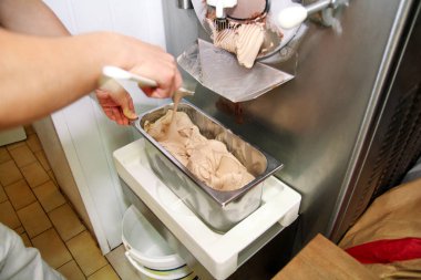 Pudra Şef üniforma içinde Ice cream maker makina üzerinde çalışıyor. Kadın fındık aromalı dondurma üreten, çelik kap içine düşüyor. İtalyan kremalı dondurma endüstriyel hazırlanması.