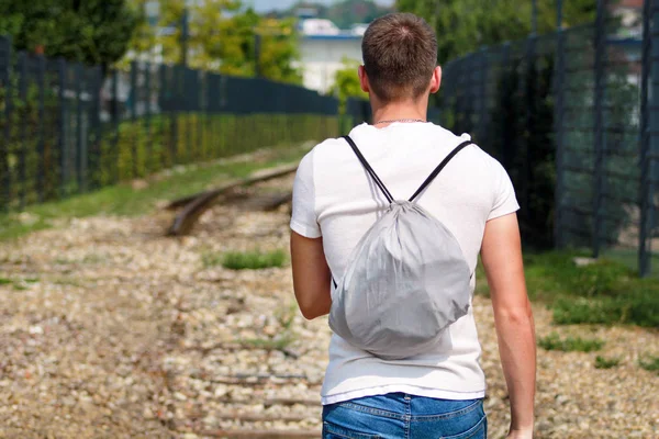 Young handsome guy walking along old railway, enjoying his surroundings on sunny day. Traveler man on railroad. Following the old railway trail. Contemplating a trip by train. City style. Adventure.