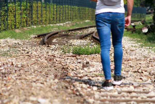 Young handsome guy walking along old railway, enjoying his surroundings on sunny day. Traveler man on railroad. Following the old railway trail. Contemplating a trip by train. City style. Adventure.