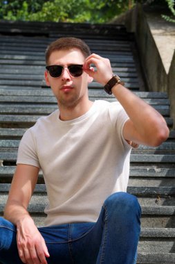 Adam oturma rahat üzerinde adımlar. Yakışıklı çocuk güneş gözlüğü ile. Erkek model poz çekim için eski merdivenlerde oturan. Mermer merdiven birinin ya da bir şey oturup... cool adam portresi.