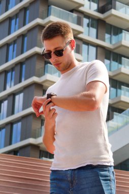 Merdivenlerin üzerinde tek başına duran adam. Güneş gözlüğü kol saati görünümlü yakışıklı çocuk. Erkek model merdivenlerinde çekimleri için poz. Merdiven, modern arka planda Bina ayrıntı üzerinde durabilen adam portresi.