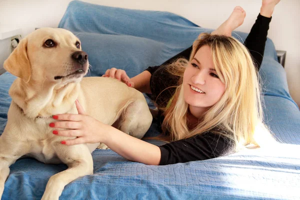 妇女与她的狗在床上在家里 在卧室放松 美丽的女孩正在玩 一起和狗在床上抚摸 黄色拉布拉多猎犬与她的主人爬上床 可爱的狗 — 图库照片