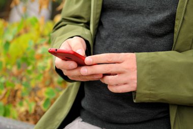 Adam cep telefonu açık havada kullanarak eller. Sosyal medya kavramı. Closeup holding ve modern smartphone ile kırmızı maske kullanarak erkek el. Adam cep telefonu akıllı izle ait diğer holding, mesaj gönderme.