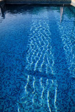 Mavi sökük su kaldırım kenarına tropikal Resort yüzme havuzunda. Yüzme Havuzu alt arka planın parçası. Açık ışık mavi havuz suyu güneş yansıması ile dalgaların. Yüzey Yüzme Havuzu.