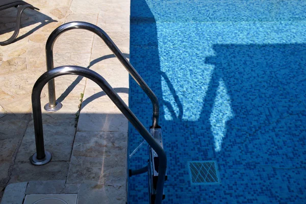 Handrail on pool. Swimming pool with stair at tropical resort. Pool handrails view. Water swimming pool with sunny reflection. Steel handrail, swimming, summer, travel. Entry to pool with handrail. — Stock Photo, Image