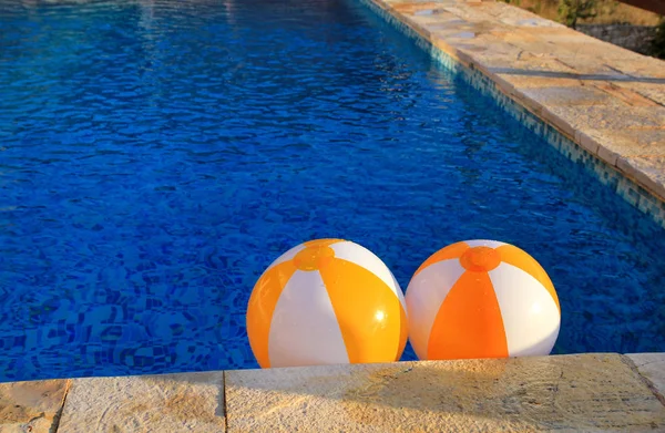 Два резиновых воздушных желто-белых шара и игрушка для бассейна в прозрачной голубой воде. Разноцветные пляжные мячи, плавающие на воде в голубом бассейне для концептуального отдыха . — стоковое фото