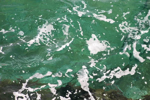 Turquesa água do mar verde com espuma do mar como fundo, close up. Superfície do mar com ondas, respingo, espuma e bolhas, textura azul abstrata e papel de parede. Belas ondas verdes com muita espuma do mar . — Fotografia de Stock