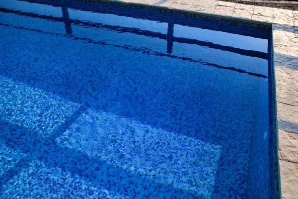 Blue ripped water in swimming pool in tropical resort with edge of pavement. Part of Swimming pool bottom background. Clear light blue pool water ripples with sun reflection. Surface of swimming pool. — Stock Photo, Image