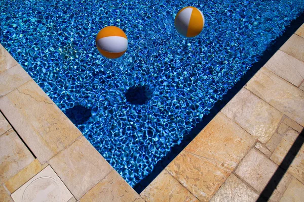 Deux boules gonflables blanches jaunes en caoutchouc et un jouet pour piscine en eau bleue transparente. Boules de plage multicolores flottant sur l'eau dans la piscine bleue pour le concept relax vacances voyage . — Photo