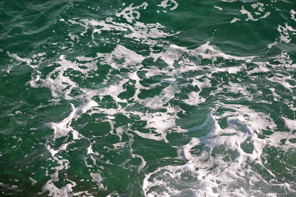 Turquoise green seawater with sea foam as background, close up. Surface of sea with waves, splash, foam and bubbles, blue abstract texture and wallpaper. Beautiful green waves with a lot of sea foam. — Stock Photo, Image