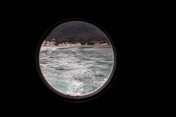 Hinged round window, storm cover on ship looking outside into Mediterranean sea. Porthole view through window on ship to turbulence made by foam of sea water from a high-speed boat on surface of sea. — Stock Photo, Image