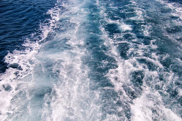 Turbulencia készült hab a tengervíz mellett egy nagysebességű hajó a tenger felszínén. Kék tenger hullámai a tengeri hab sok. Tenger hullámai, splash, háttérkép, kék háttér, hab és buborékok felület. — Stock Fotó