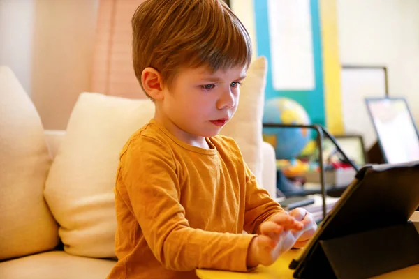 Niño usando tableta pc en la cama en casa. Lindo chico en el sofá está viendo dibujos animados, jugando y aprendiendo de la computadora portátil. Educación, diversión, ocio, felicidad, tecnología informática moderna y comunicación . — Foto de Stock