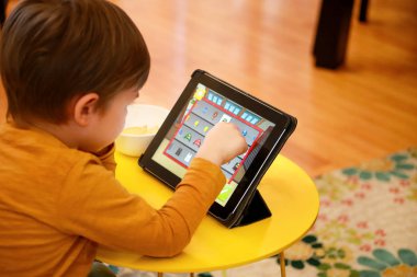 Çocuk evde yatakta Tablet PC'yi kullanma. Divan sevimli çocuk çizgi film izlemek, oyun oynamak ve dizüstü öğrenme. Eğitim, eğlence, eğlence, mutluluk, modern bilgisayar teknoloji ve iletişim.