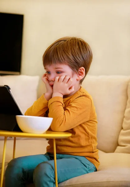 Ребенок, используя планшетный компьютер на кровати дома. Симпатичный мальчик на диване смотрит мультфильм, играет в игры и учится на ноутбуке. Образование, развлечения, досуг, счастье, современные компьютерные технологии и коммуникации . — стоковое фото