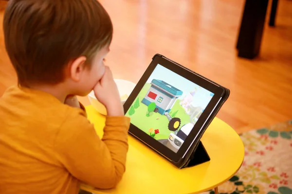 Çocuk evde yatakta Tablet PC'yi kullanma. Divan sevimli çocuk çizgi film izlemek, oyun oynamak ve dizüstü öğrenme. Eğitim, eğlence, eğlence, mutluluk, modern bilgisayar teknoloji ve iletişim.