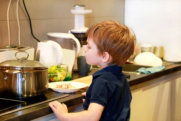 Portret van kind in keuken. Schattige kleine jongen, spelen in de keuken. Jonge jongen is hongerig, kijkt naar en controles is het klaar lunch. Kindertijd, eten en drinken concept. Onderwijs, plezier, vrije tijd, geluk. — Stockfoto