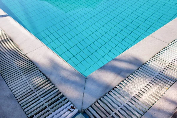 Blue ripped water in swimming pool in tropical resort with edge of pavement. Part of Swimming pool bottom background. Clear light blue pool water ripples with sun reflection. Surface of swimming pool.