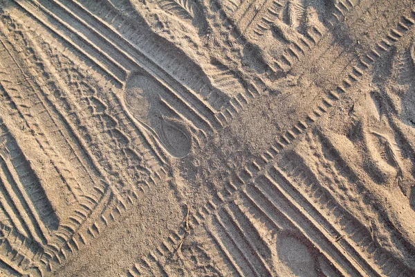 Utwory w piasku. Część odbitek i torów opon, stóp, stóp, słonecznych kapci morskich w piasku plażowym. Tekstura, materiał, wzór, tło i tapeta z piasku. Przecinanie gąsienic pojazdu w miękkim piasku. — Zdjęcie stockowe