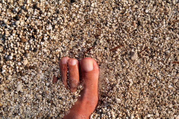 Top view of man standing bare feet on beach. Texture of bottom, leg and foot of man drowning with sweeping colorful stone below on rocky stones beach in sea with waves and foam, water ripples of sea. — Stock Photo, Image