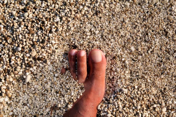 Top view of man standing bare feet on beach. Texture of bottom, leg and foot of man drowning with sweeping colorful stone below on rocky stones beach in sea with waves and foam, water ripples of sea. — Stock Photo, Image