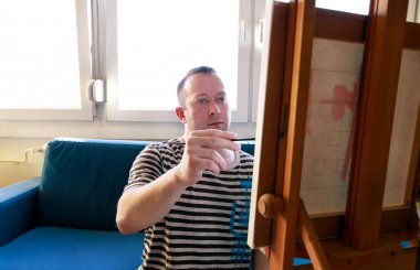 Erkek sanatçı ressam sanat boya atölyesinde ahşap çizim tahtası şüskül üzerinde tuval ile atölyede çalışıyor. Boya fırçası ile sanatçının portresi yağlı boyalar ile tuval üzerine boyama olduğunu. Yaratıcılık kavramı.