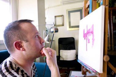 Erkek sanatçı ressam sanat boya atölyesinde ahşap çizim tahtası şüskül üzerinde tuval ile atölyede çalışıyor. Boya fırçası ile sanatçının portresi yağlı boyalar ile tuval üzerine boyama olduğunu. Yaratıcılık kavramı.