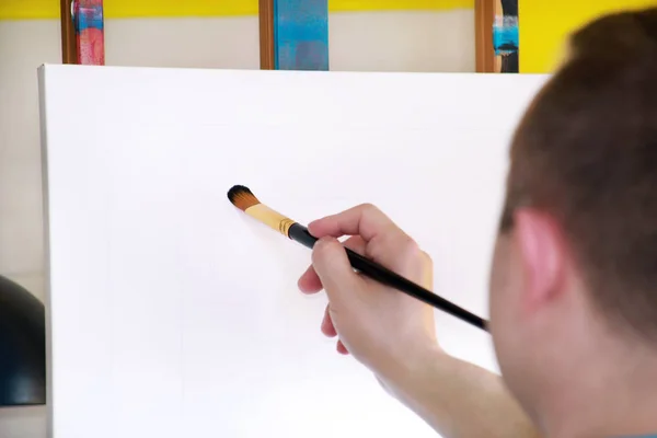 Artista masculino pintor trabalhando em oficina com tela em madeira desenho cavalete no estúdio de pintura de arte. Retrato de artista com pincel é pintura sobre tela com tintas a óleo. Conceito de criatividade . — Fotografia de Stock