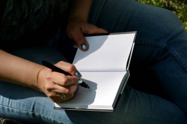 Çimenlerin üzerinde oturan kadın ve öğrenci, not defterinde notlar alır, öğrenir ve düşünce yazar, kitap yazar, ödev yaparak ve düşünerek final sınavlarını hazırlıyor, not defterine bir şeyler yazıyor..