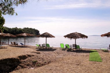 Deniz yoluyla plajda yalnız hasır güneş şemsiyesi. Doğal bambu güneşlikler, yaz şemsiye şemsiyesi, şezlong, masa, şezlong, şezlong ve şemsiye okyanus plajda güneşlenmek için turistlerbekliyor.