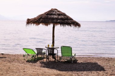 Deniz yoluyla plajda yalnız hasır güneş şemsiyesi. Doğal bambu güneşlikler, yaz şemsiye şemsiyesi, şezlong, masa, şezlong, şezlong ve şemsiye okyanus plajda güneşlenmek için turistlerbekliyor.