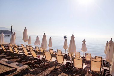 Boş şezlong, şezlong, şemsiye, yazlık şemsiye, şezlong, masa, şezlong ile insanlar olmadan kumlu plajda sabahın erken saatlerinde turistleri bekliyor.