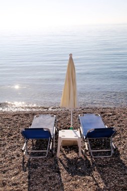 Boş şezlong, şezlong, şemsiye, yazlık şemsiye, şezlong, masa, şezlong ile insanlar olmadan kumlu plajda sabahın erken saatlerinde turistleri bekliyor.