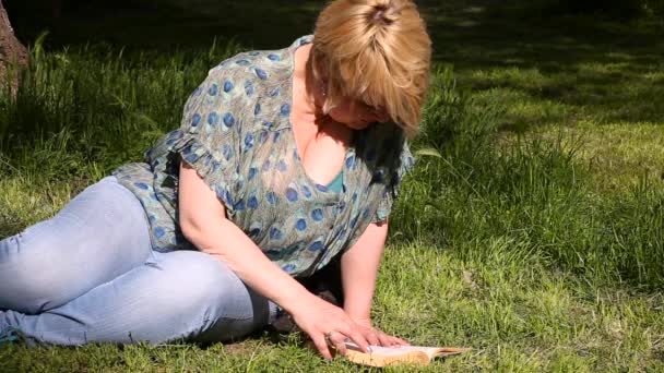 여성은 잔디에 공원에서 흥미로운 여자는 앉아서 공부하고 아름다운 환경에서 즐긴다 — 비디오
