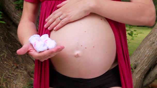 孕妇抱着婴儿袜子 拥抱和抚摸怀孕的肚子 未来的妈妈和父母正在等待宝宝 爱和幸福 出生期望概念 — 图库视频影像