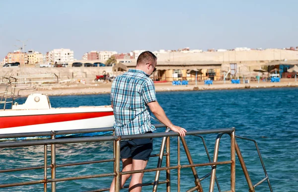 Ritratto di turista e viaggiatore è in posa e camminare sul molo della spiaggia, gode di sole e vista sul paesaggio marino. Uomo con occhiali da sole in vacanza in estate in hotel resort sulla piattaforma molo mare . — Foto Stock