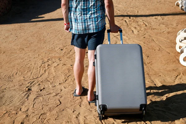 남성 관광객과 여행자 산책과 호텔 리조트의 모래 해변에서 자신의 여행 가방을 당겨. 여름에 휴가에 잘 생긴 남자, 그는 짐, 호텔 숙박 시설에 가고. 휴일 개념. — 스톡 사진