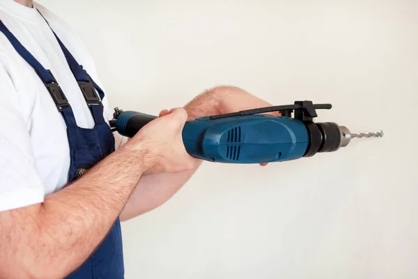 Construction worker and handyman works on renovation of apartment. Builder with blue electric drill drills a nail hole into wall of construction site. House renovation concept. Construction tools.