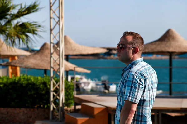 Turist ve gezgin portresi poz ve Mısır'da otel tesisi güzel plajda izliyor, güneş ve deniz manzara görünümünde sahiptir. Yaz aylarında tatilde güneş gözlüğü ile Yakışıklı adam. — Stok fotoğraf