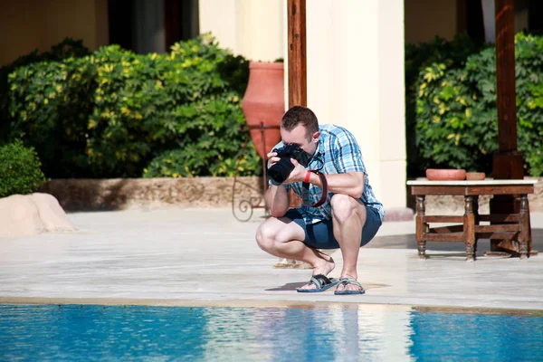 Profesyonel fotoğrafçı, turist ve otel resort yüzme havuzu nda gezgin, o fotoğraf çekerek, kamera ile su ve çevre fotoğrafçılığı yapıyor. Yakışıklı adam yaz tatilde. — Stok fotoğraf