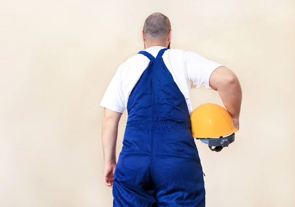 İnşaat işçisi ve tamirci daire yenileme üzerinde çalışıyor. Koruyucu üniforma ve ekipman ile şantiyede Oluşturucu, o takım elbise ile, tulum ve sarı kask elinde tutarak. — Stok fotoğraf