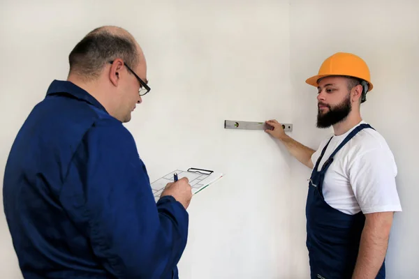 Ingeniero, contratista y director de proyecto con su colega, trabajador de la construcción, manitas y constructor está midiendo el espacio de la pared para la renovación utilizando la herramienta de nivel espiritual, comprobando en el plano del apartamento . — Foto de Stock