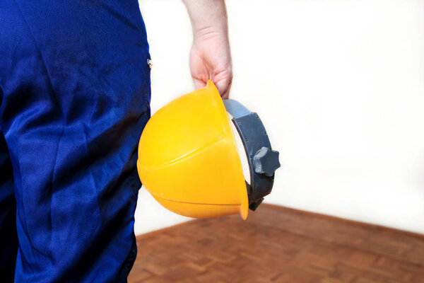 Строитель и мастер работает над ремонтом квартиры. Строитель на строительной площадке в защитной форме и снаряжении, он с костюмом, покрывалом и желтым шлемом держит в руке
.