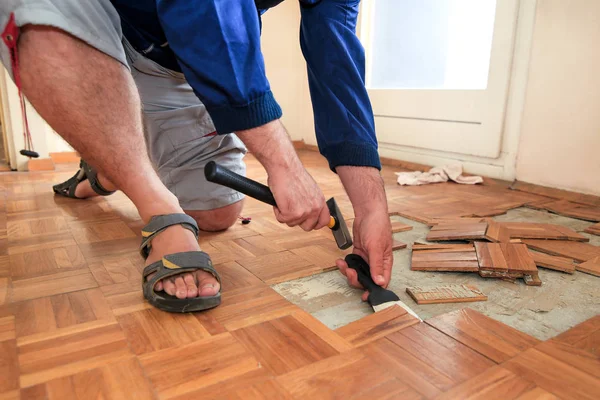 Bouwvakker en constructeur werkt aan renovatie van appartement. Klusjesman is het verwijderen van oude houten parketvloeren met behulp van gele hamer en schrapen gereedschap. Bouwer ontmantelt parketvloer. — Stockfoto